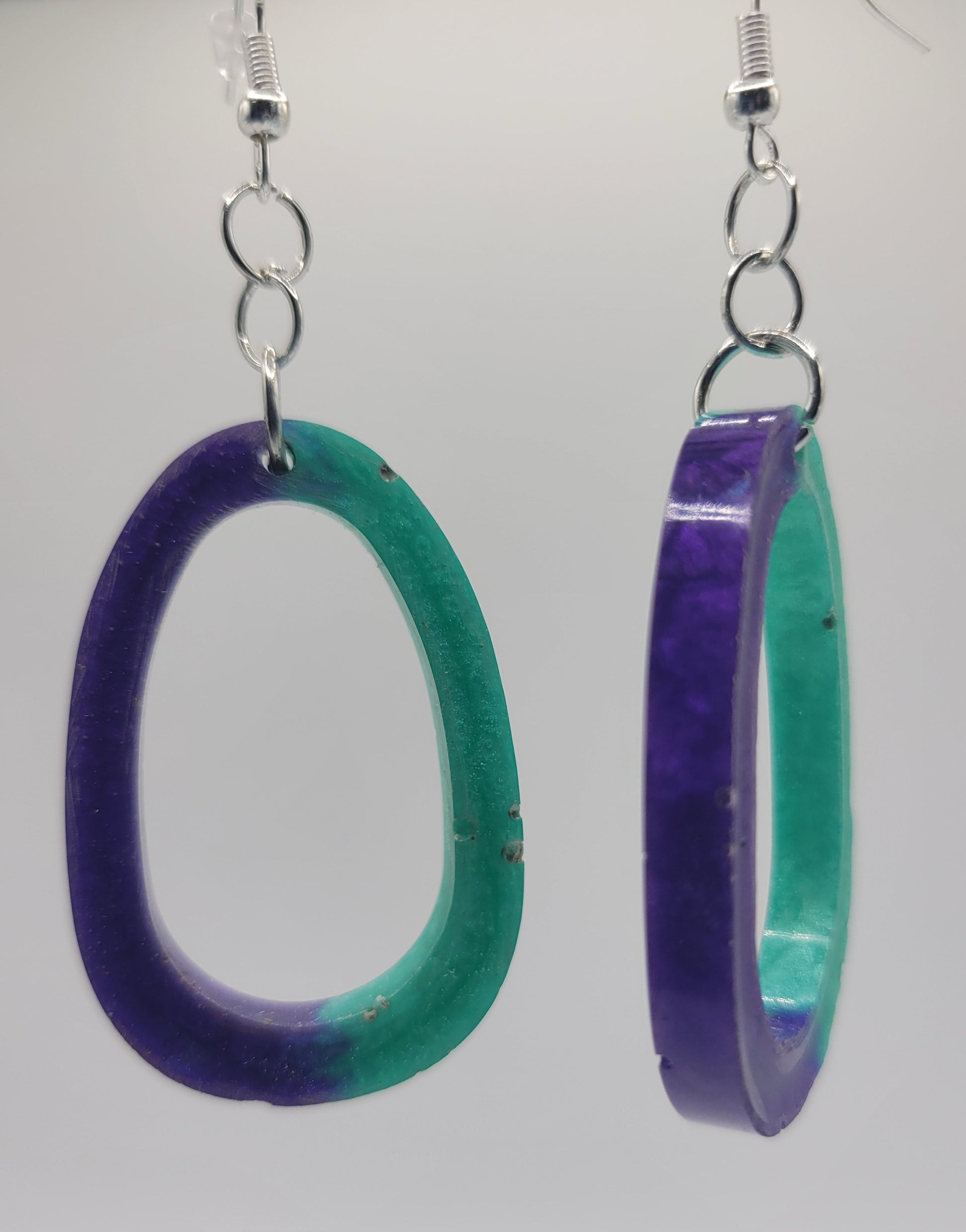 Two green and purple circular earrings on a white background