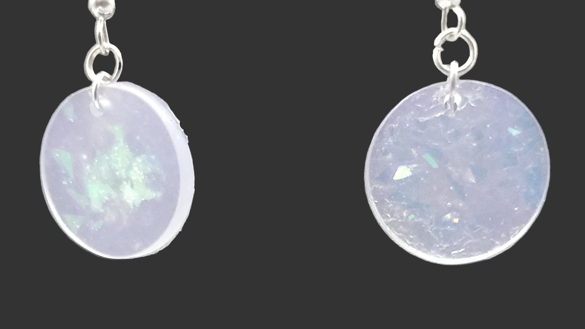 Pair of round earrings with a light purple or lavender color on a gray background