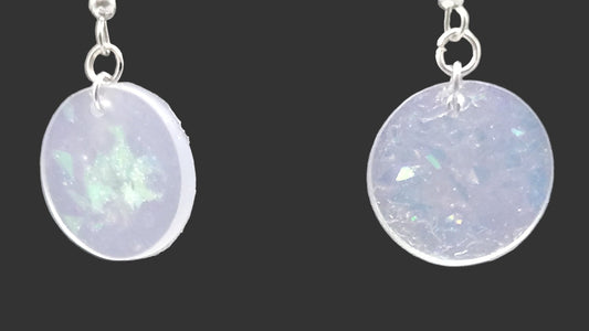 Pair of round earrings with a light purple or lavender color on a gray background