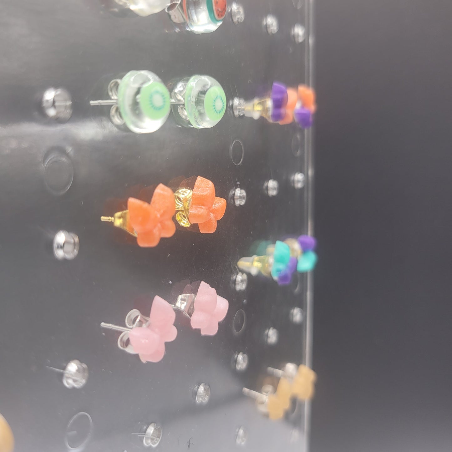 Assorted colorful earrings on a clear stand with a dark background