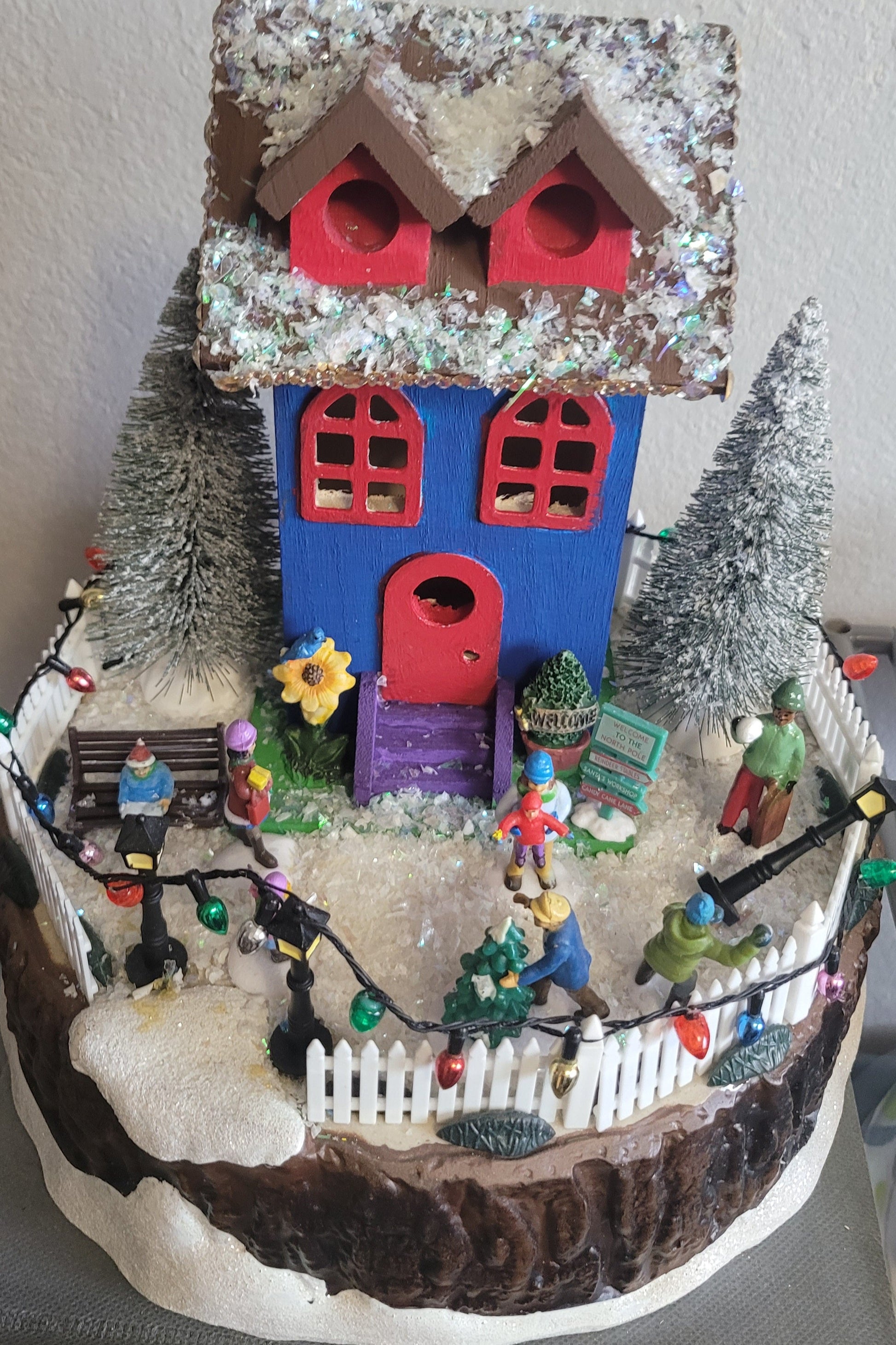 Decorative model of a house with small figures and Christmas lights on a white background