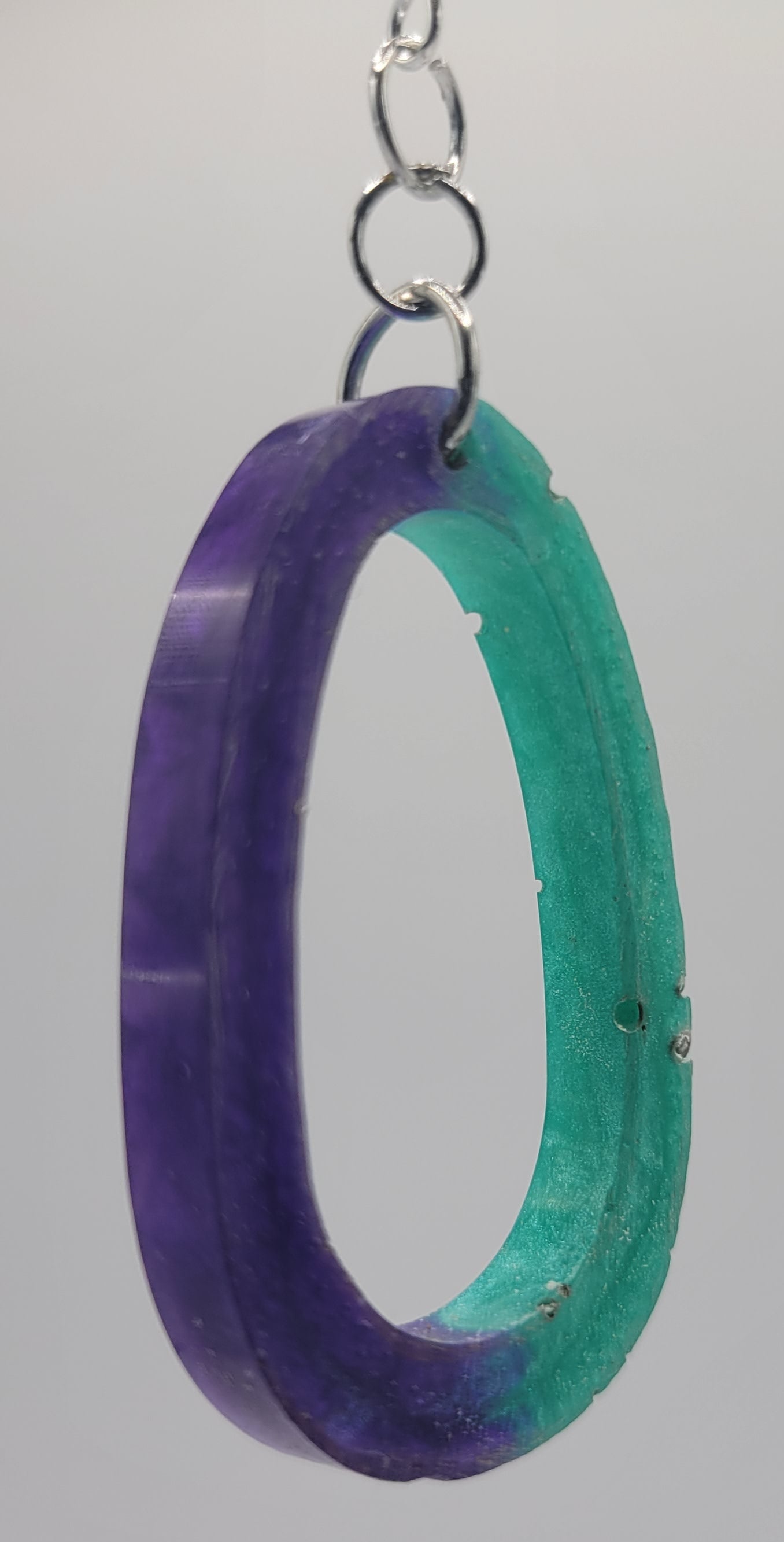Two interlocking purple and green rings on a chain against a plain background