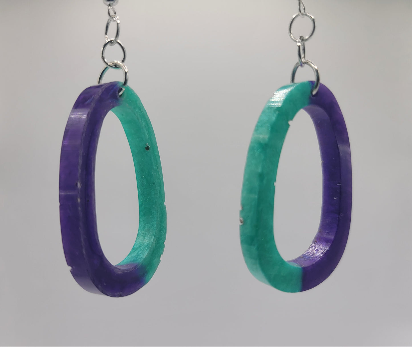 Pair of earrings with purple and green oval design on a gray background