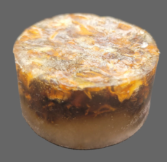 Round, brownish soap puck with a textured flower petal surface on a black backround