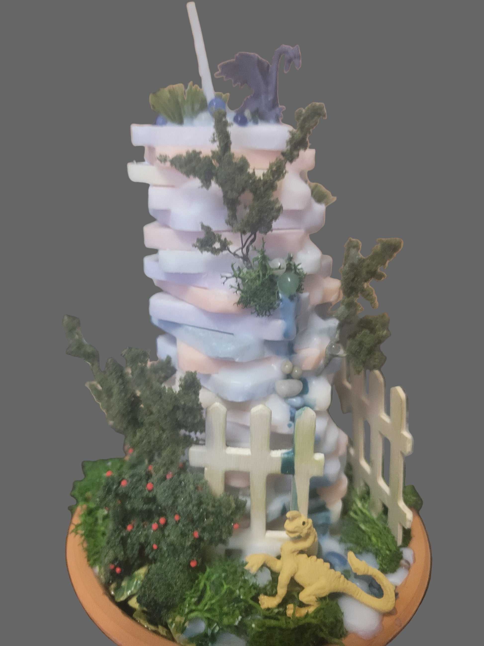Miniature garden scene with a fence, plants, and a dragon figurines guard the candle mountain